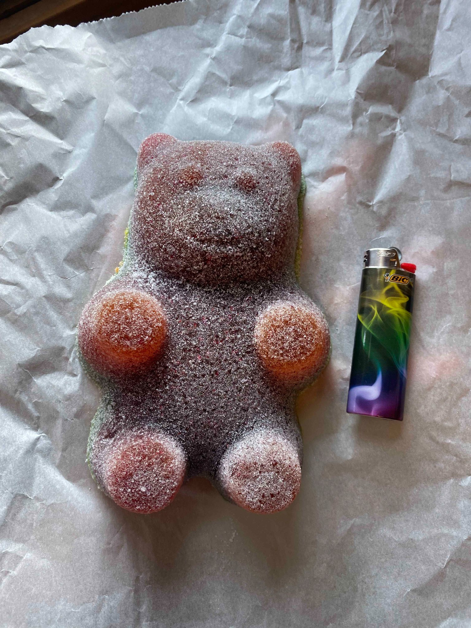 Oversized sugar‑coated gummy bear with lighter for scale